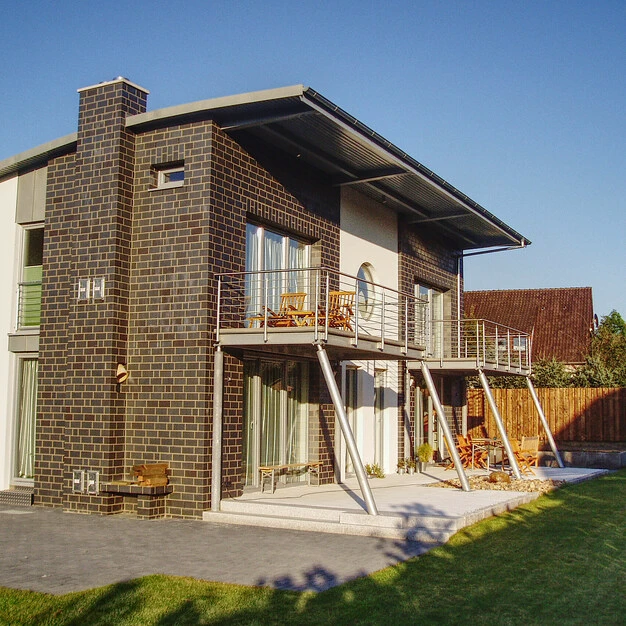 Modernes Backsteinhaus mit zwei Stockwerken Balkonen und viel Glas im sonnigen Garten