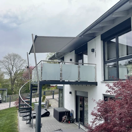 Modernes Wohnhaus mit Balkon großen Fenstern und auffälligem rotem Strauch rechts im Vordergrund