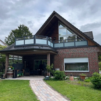 Zeitgemäßes Backsteinhaus mit großen Fenstern einem Balkon und einem gepflasterten Gartenweg