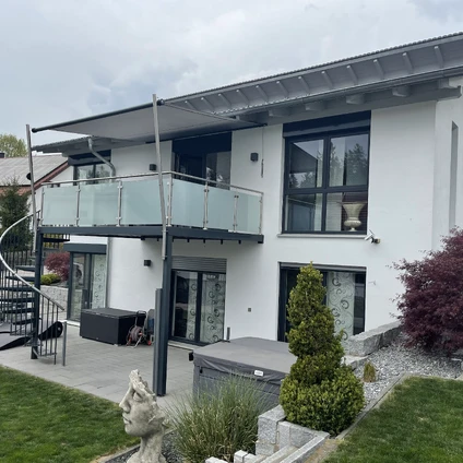 Modernes weißes Haus mit Balkon großen Fenstern und gepflegter Gartenanlage