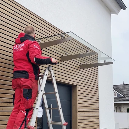 Arbeiter montiert modernes Glasdach an der Fassade eines Holzhausbaus auf einer Leiter